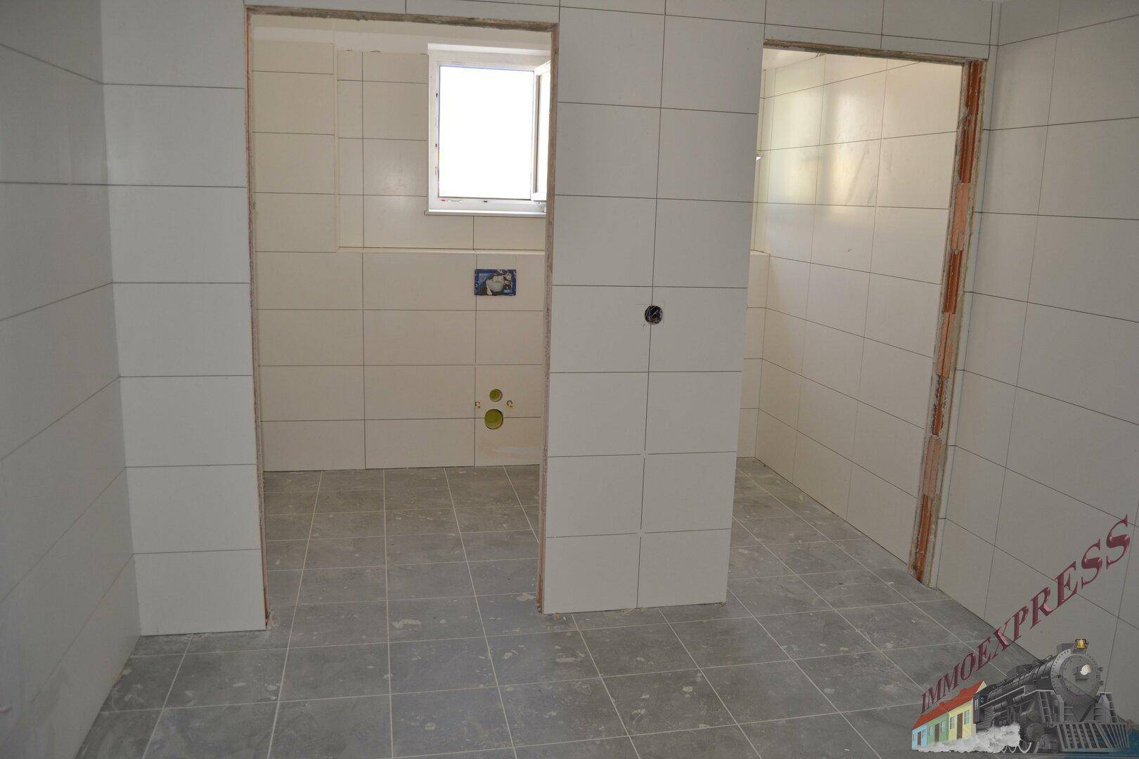 Unfertiges Badezimmer mit weißen Wandfliesen und grauen Bodenfliesen, bereit für die Installation.