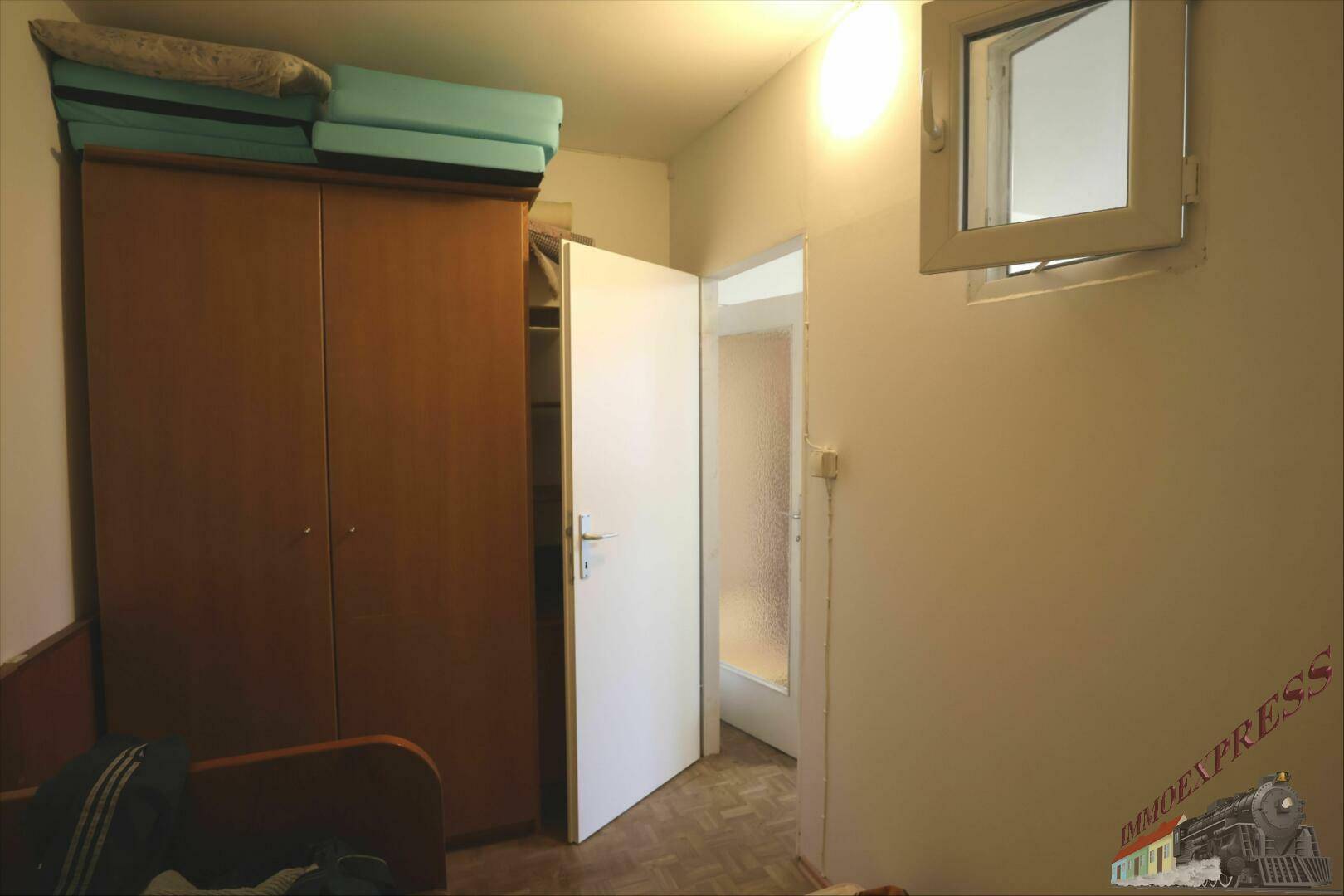 Schlafzimmer mit Kleiderschrank und kleinem Fenster, bietet einfachen Wohnkomfort.