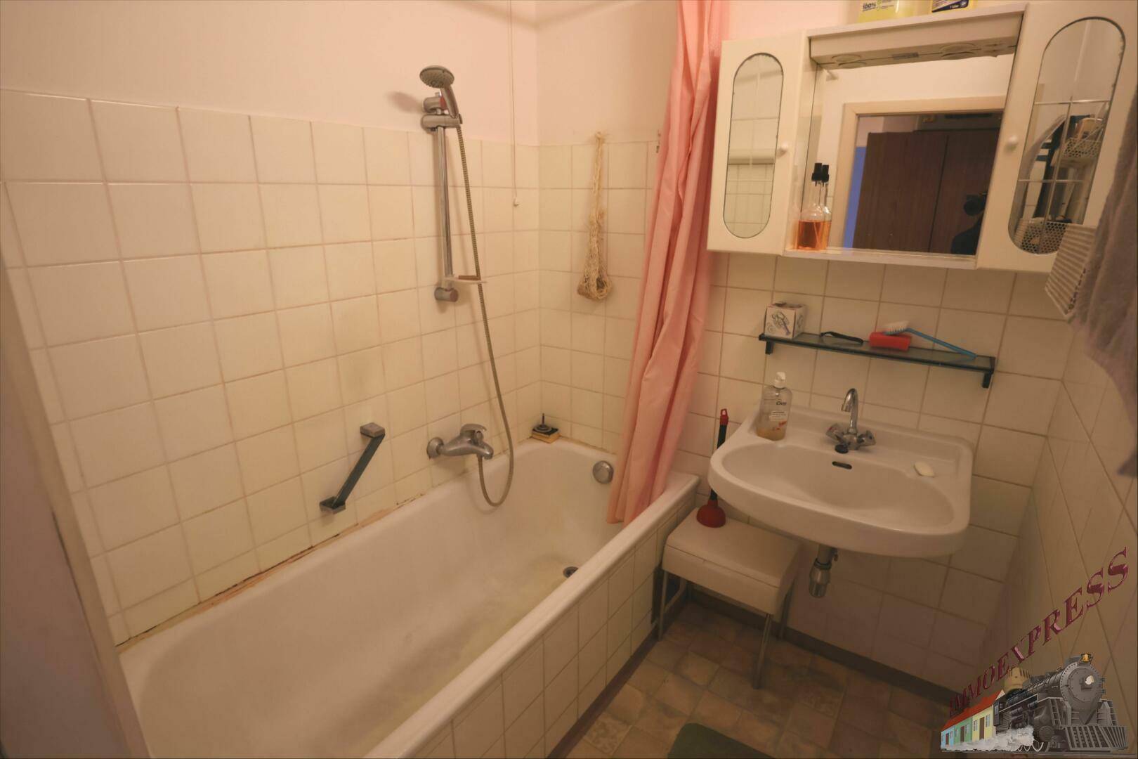 Einfaches Badezimmer mit Badewanne, Dusche und Waschbecken, gefliest in hellem Beige.