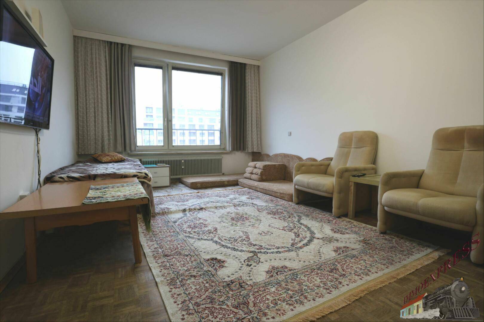 Geräumiges Wohnzimmer mit Teppich, Sitzmöbeln und großem Fenster mit Stadtblick.