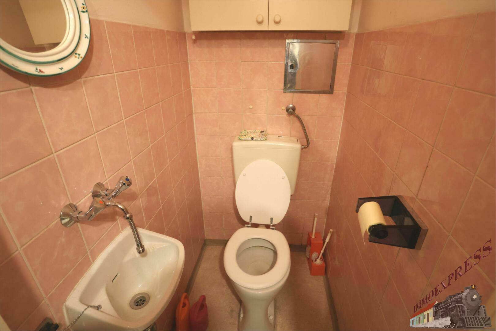 Separate Toilette mit rosa Fliesen, WC und kleinem Handwaschbecken.