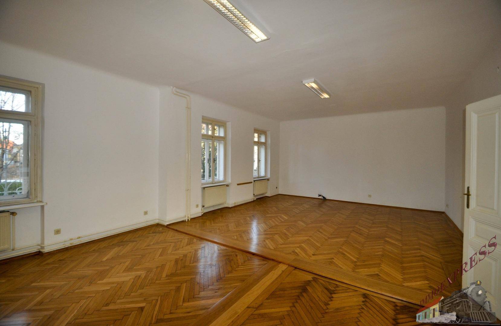 Geräumiger Raum mit Fischgrätparkett, mehreren Fenstern und weiß gestrichenen Wänden.