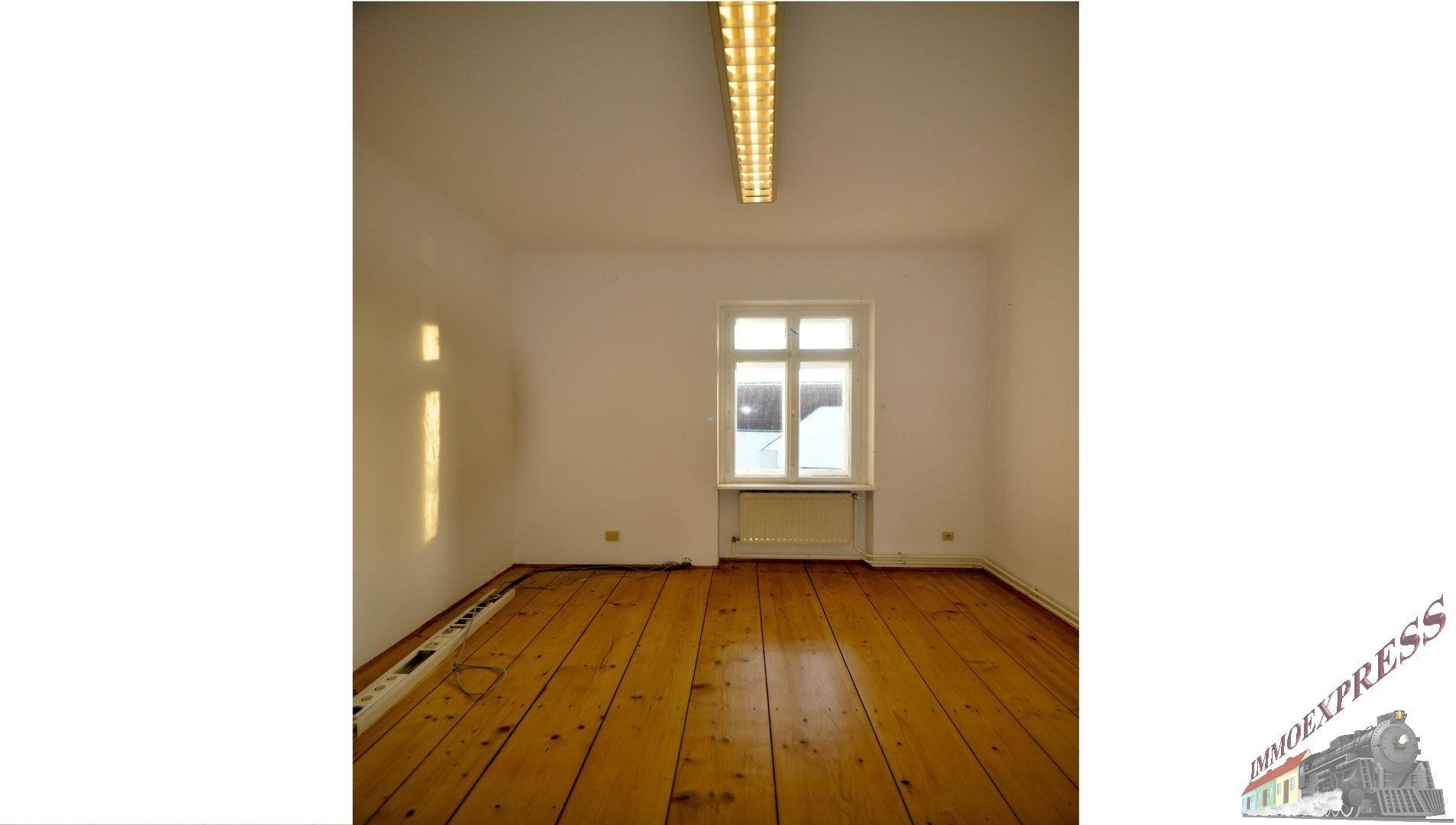 Heller Raum mit Dielenboden, einem Fenster und weiß gestrichenen Wänden.