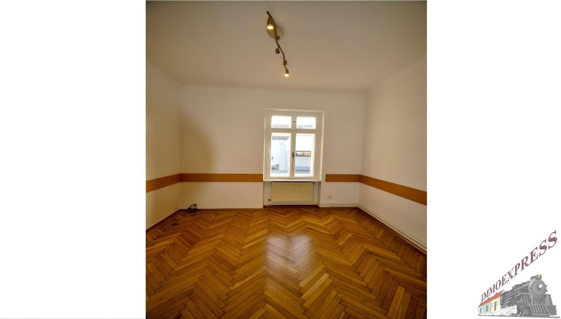Heller Raum mit Fischgrätparkett, einem Fenster und einer dekorativen braunen Wandleiste.