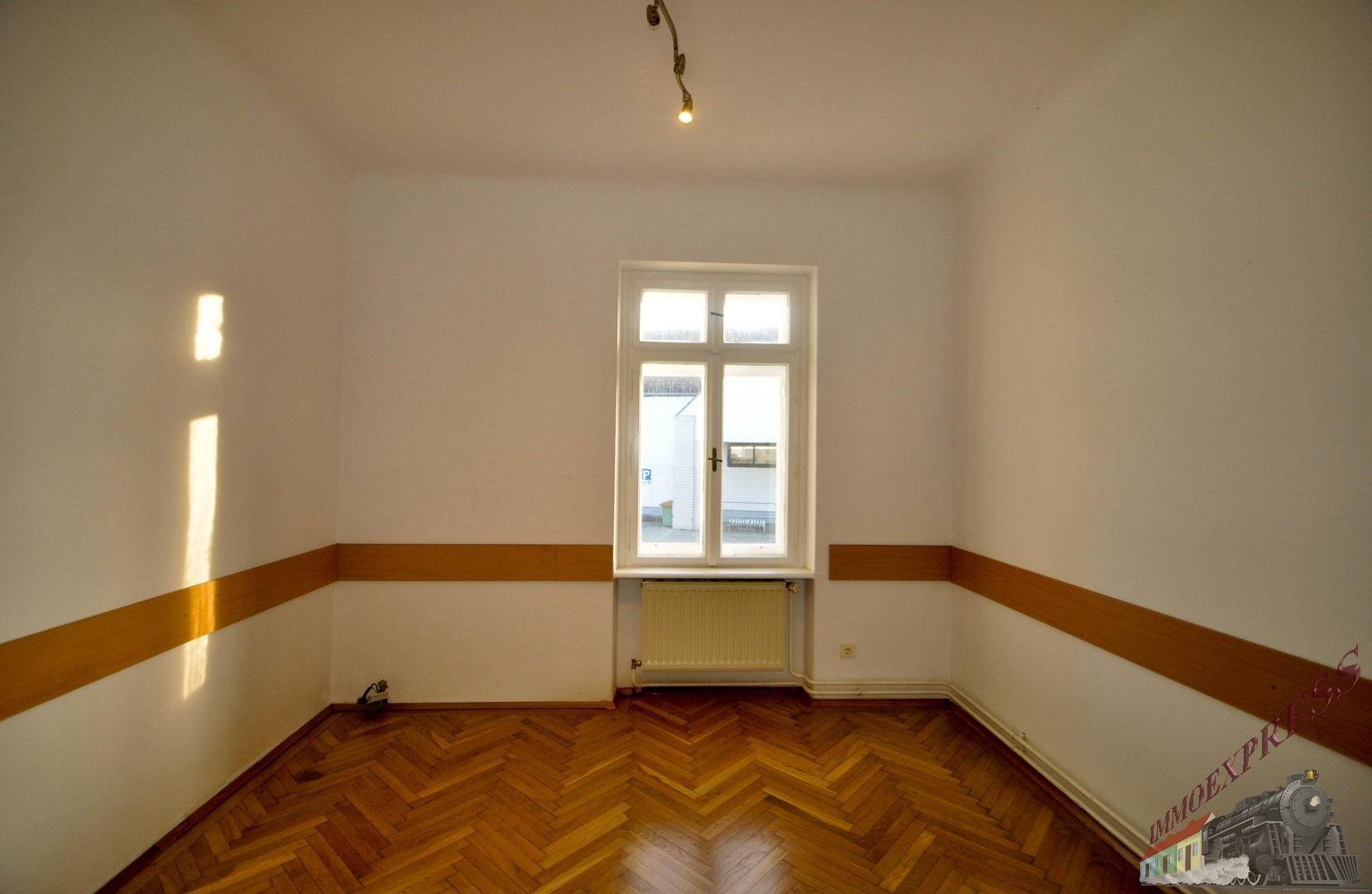 Heller Raum mit Fischgrätparkett, einem Fenster und einer dekorativen braunen Wandleiste.
