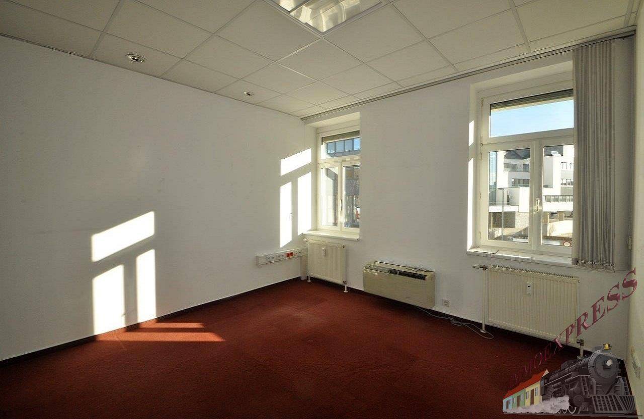 Geräumiges Büro mit zwei großen Fenstern, die viel Tageslicht hereinlassen, und einem roten Teppichboden.