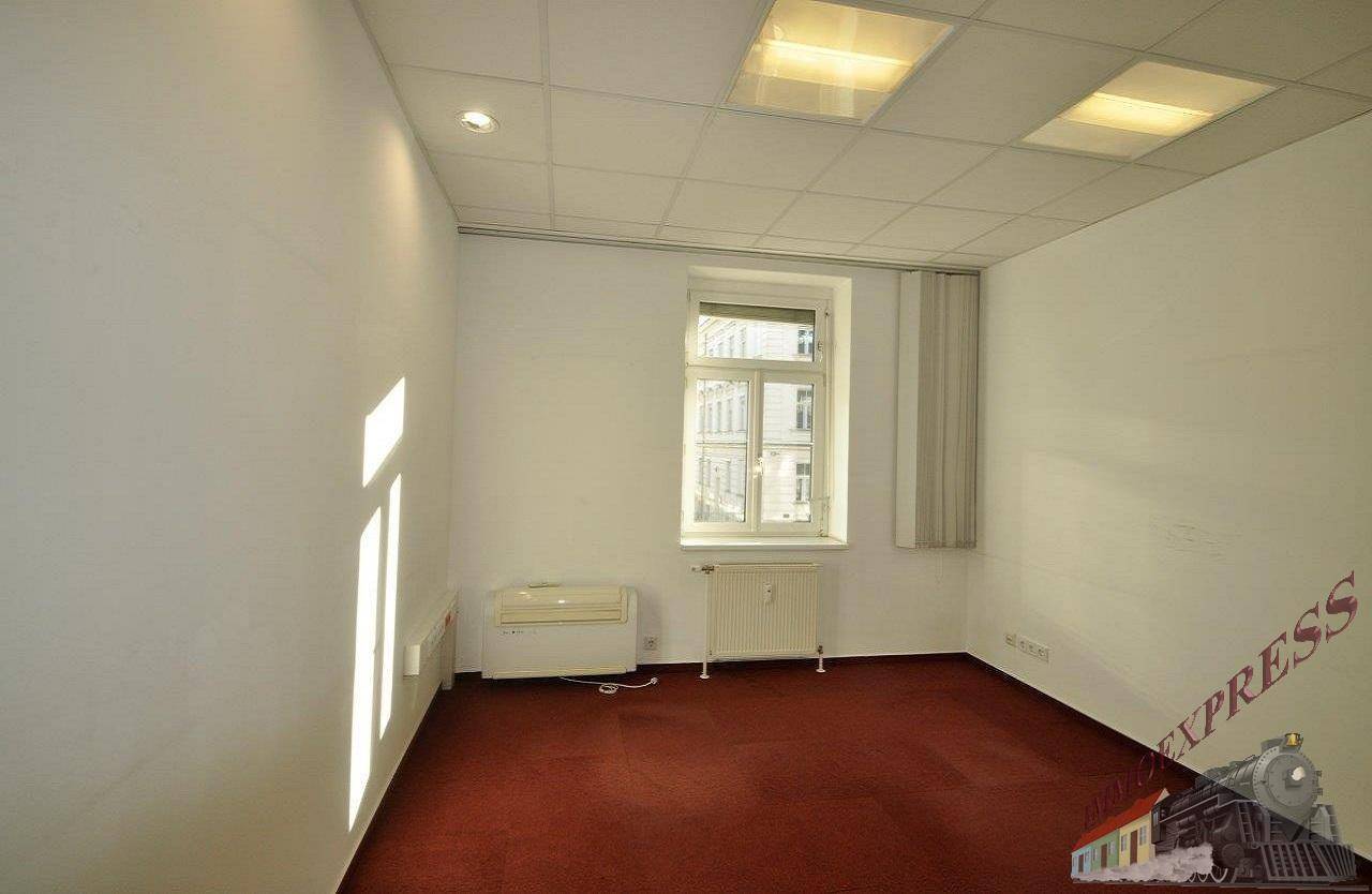 Einzelbüro mit einem Fenster, das Tageslicht spendet, rotem Teppichboden und einer schlichten Einrichtung.