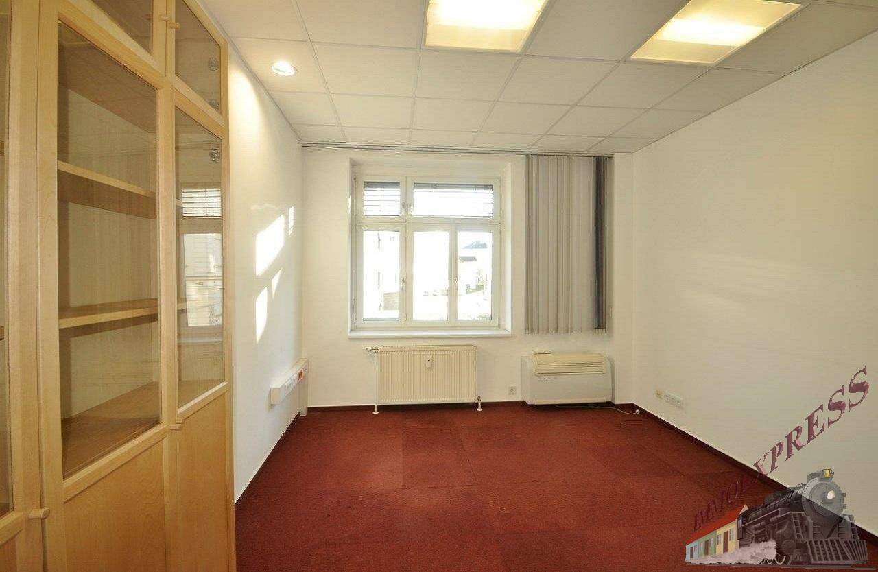 Büroraum mit einem Holzschrank, einem Fenster für Tageslicht und einem roten Teppichboden.