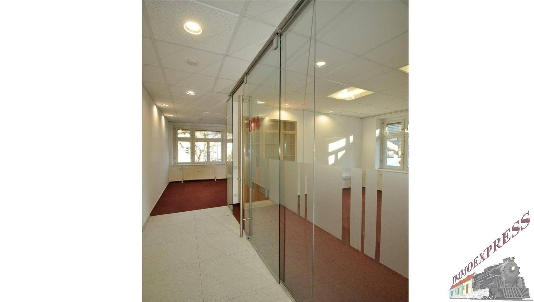 Heller Flur mit Glaswänden, die zu den Büroräumen führen, und einem hellen Fliesenboden.
