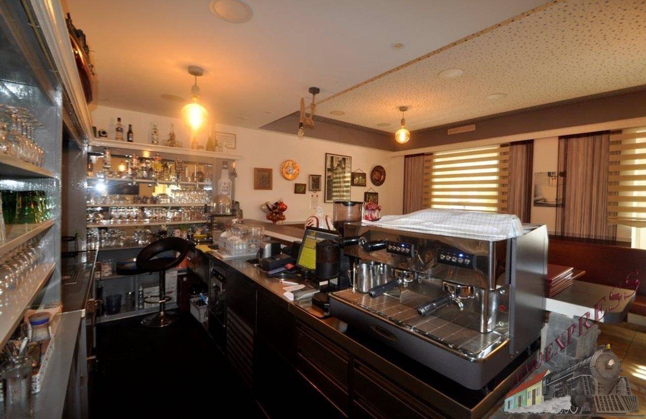 Blick hinter die Bar mit professioneller Espressomaschine und Sitzbereich im Hintergrund für Gäste.