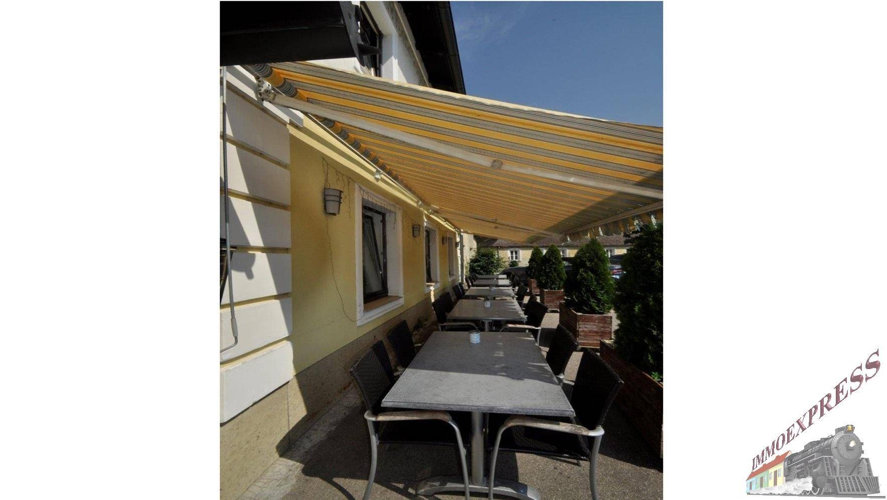 Außenbereich mit Tischen, Stühlen und einer gestreiften Markise für angenehmen Schatten.