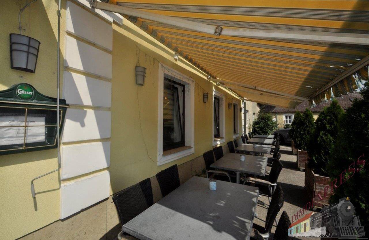 Terrasse mit weiteren Sitzgelegenheiten und Blick auf die Gebäudefassade, ideal für warme Tage.