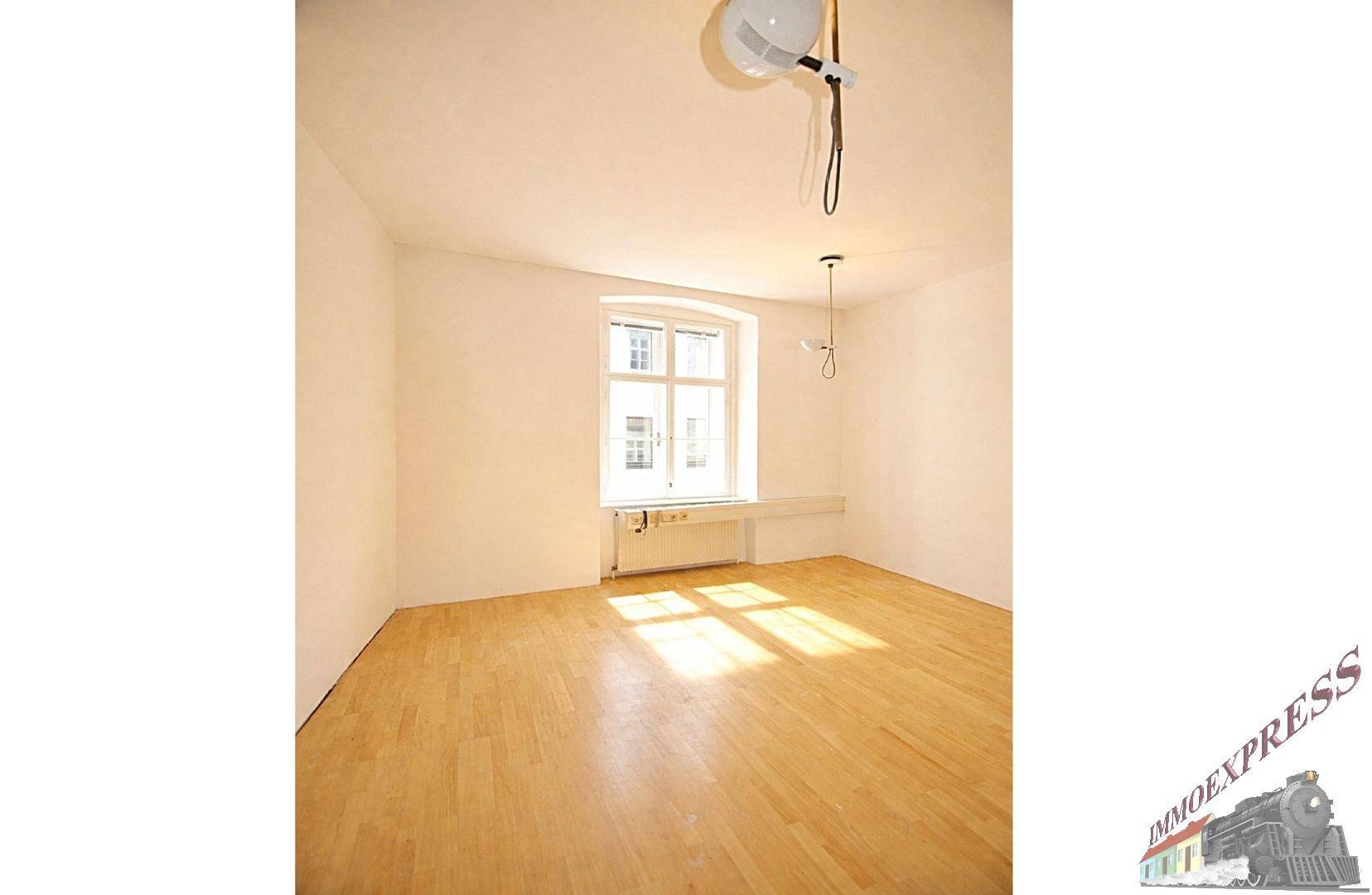 Heller und sauberer Büroraum mit einem Fenster, das viel Tageslicht spendet, und Holzparkettboden.