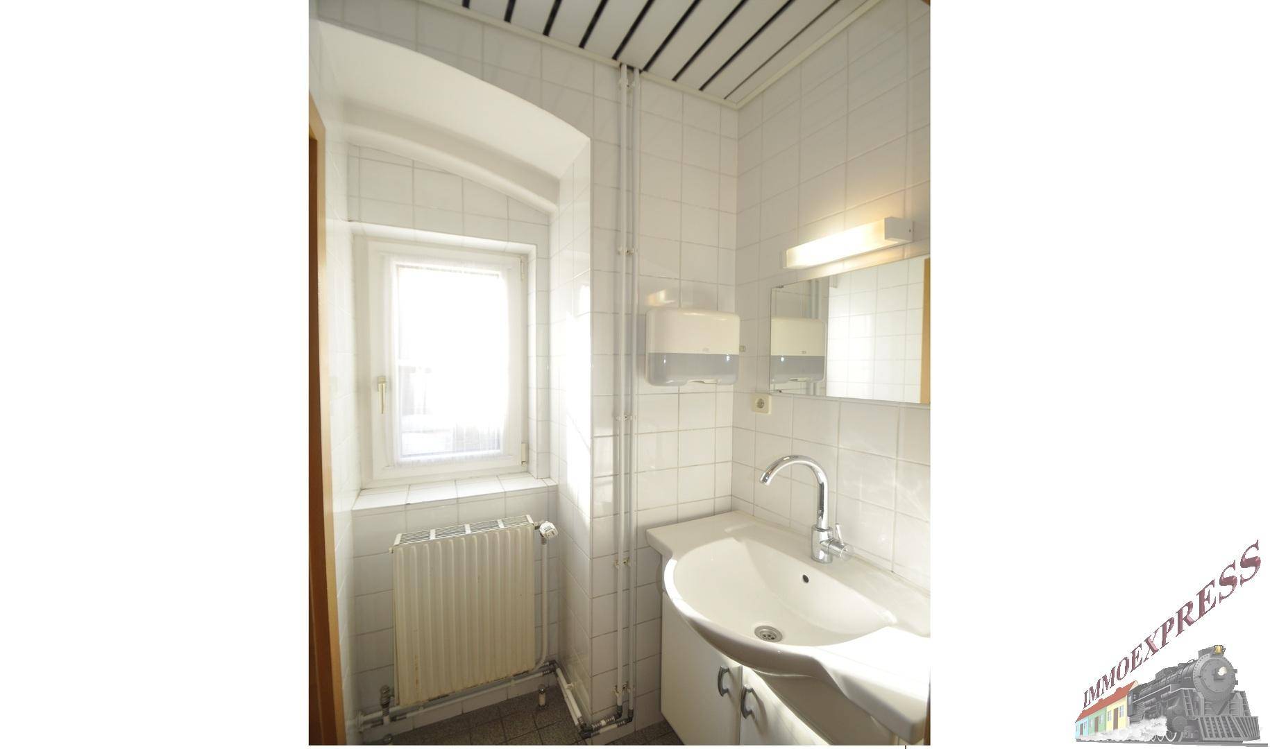 Helles Badezimmer mit Waschbecken, Spiegel und einem Fenster für natürliche Belüftung.