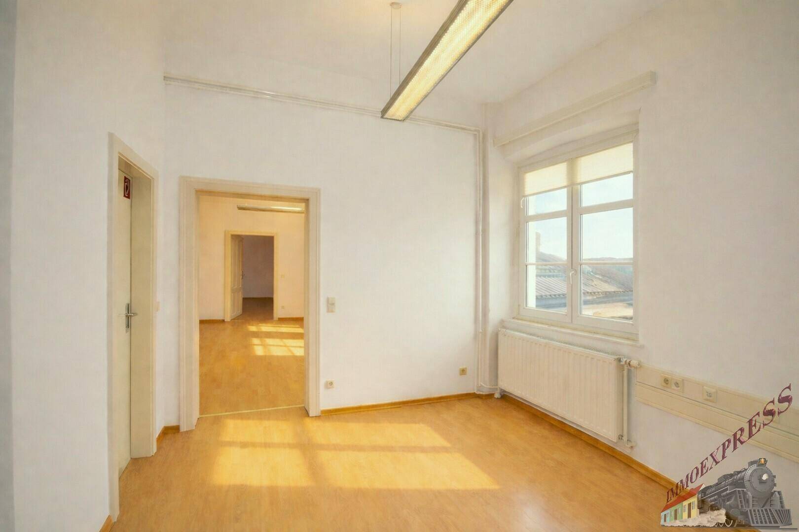 Geräumiger, heller Raum mit Holzboden und großen Fenstern, der viel Tageslicht hereinlässt und vielseitig nutzbar ist.