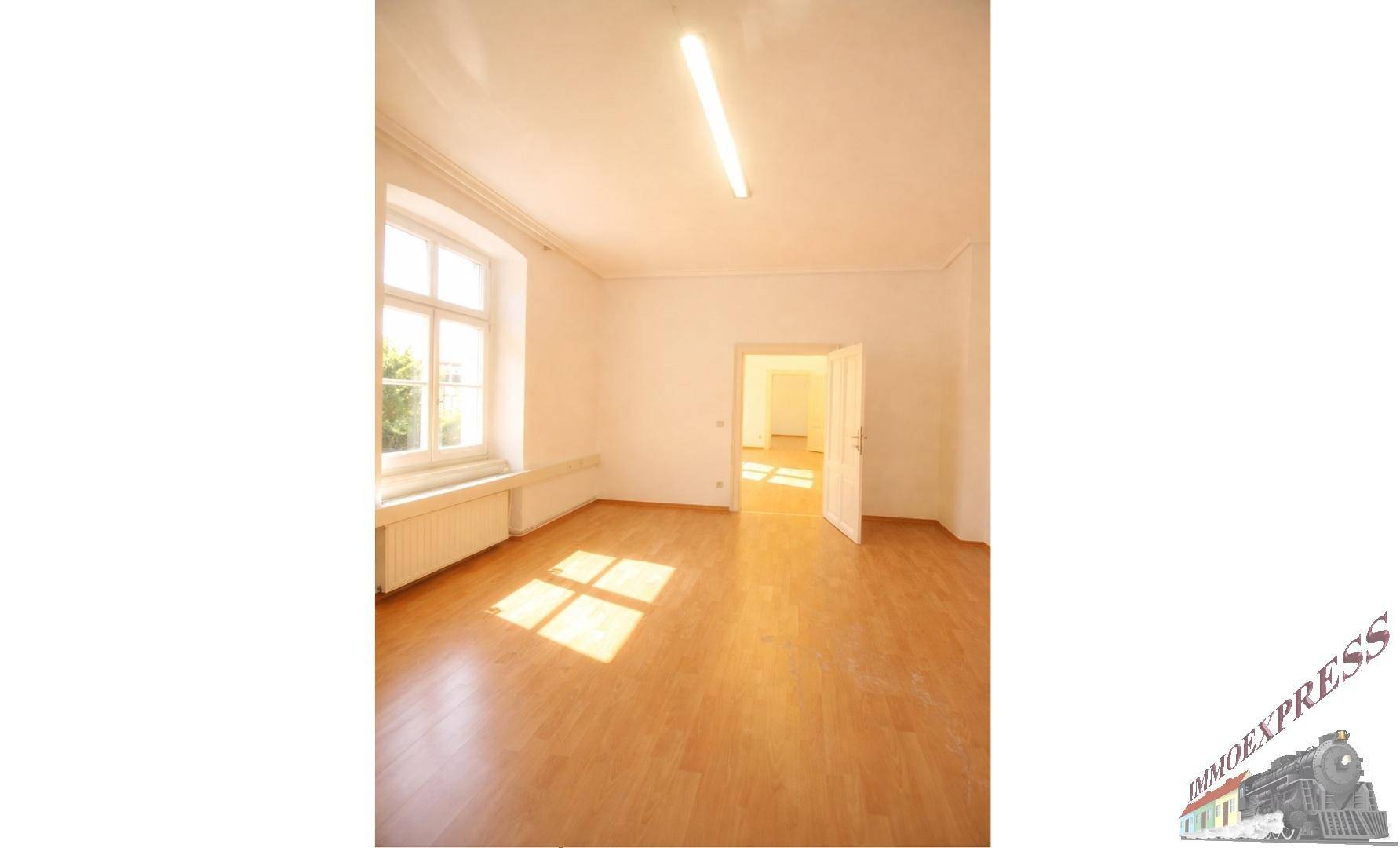 Heller Raum mit Holzboden und einem großen Fenster, das den Raum mit natürlichem Licht durchflutet.
