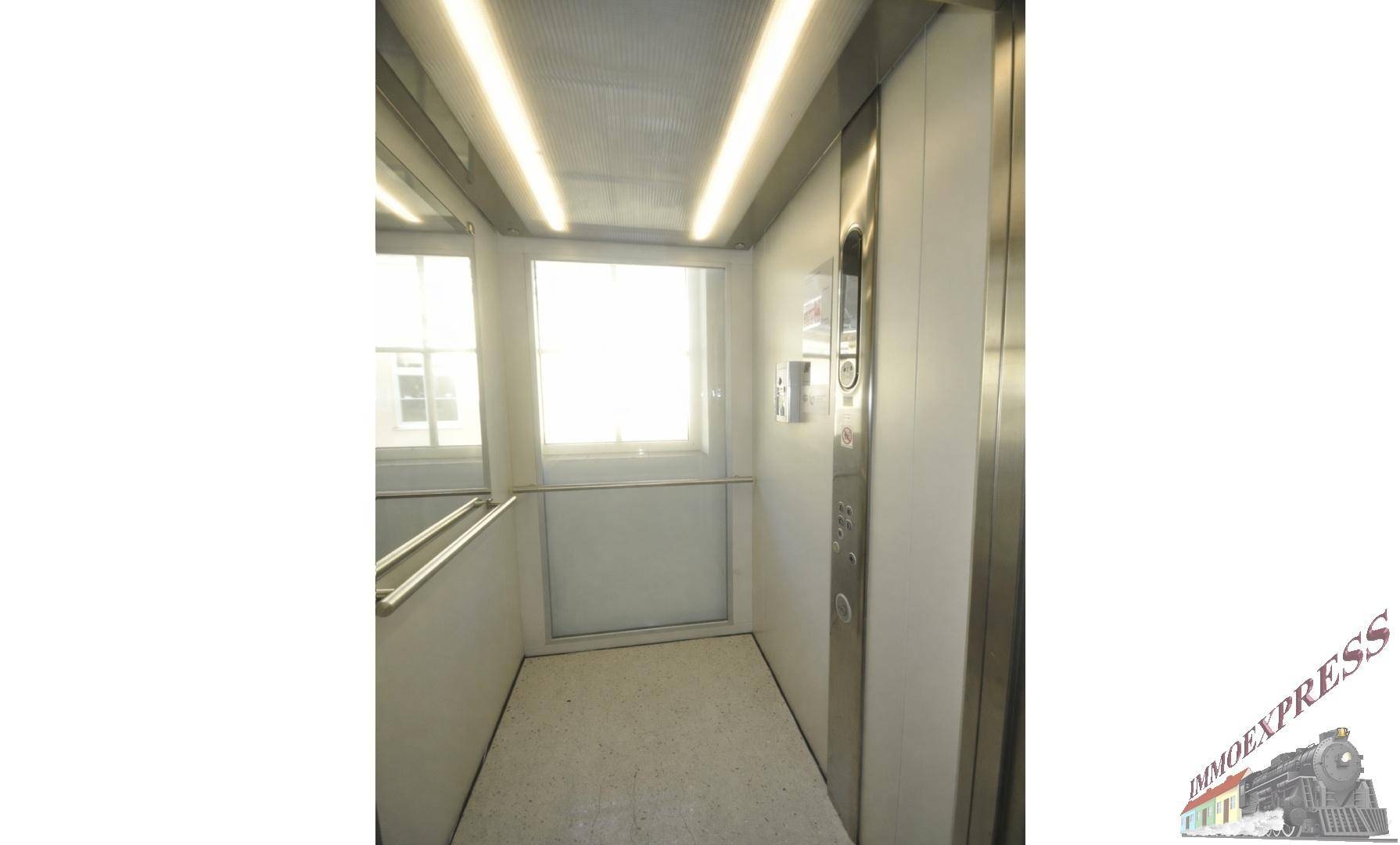 Moderner Aufzug mit Edelstahlpaneelen, einem Fenster und heller Beleuchtung, der Zugang zu den Etagen bietet.