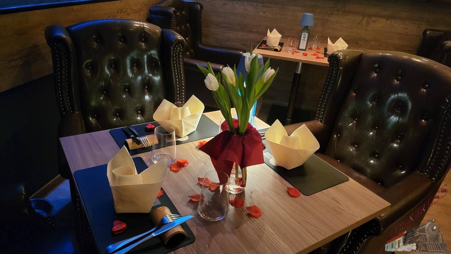 Nahaufnahme eines romantisch gedeckten Tisches für zwei Personen mit Blumen und Rosenblättern.