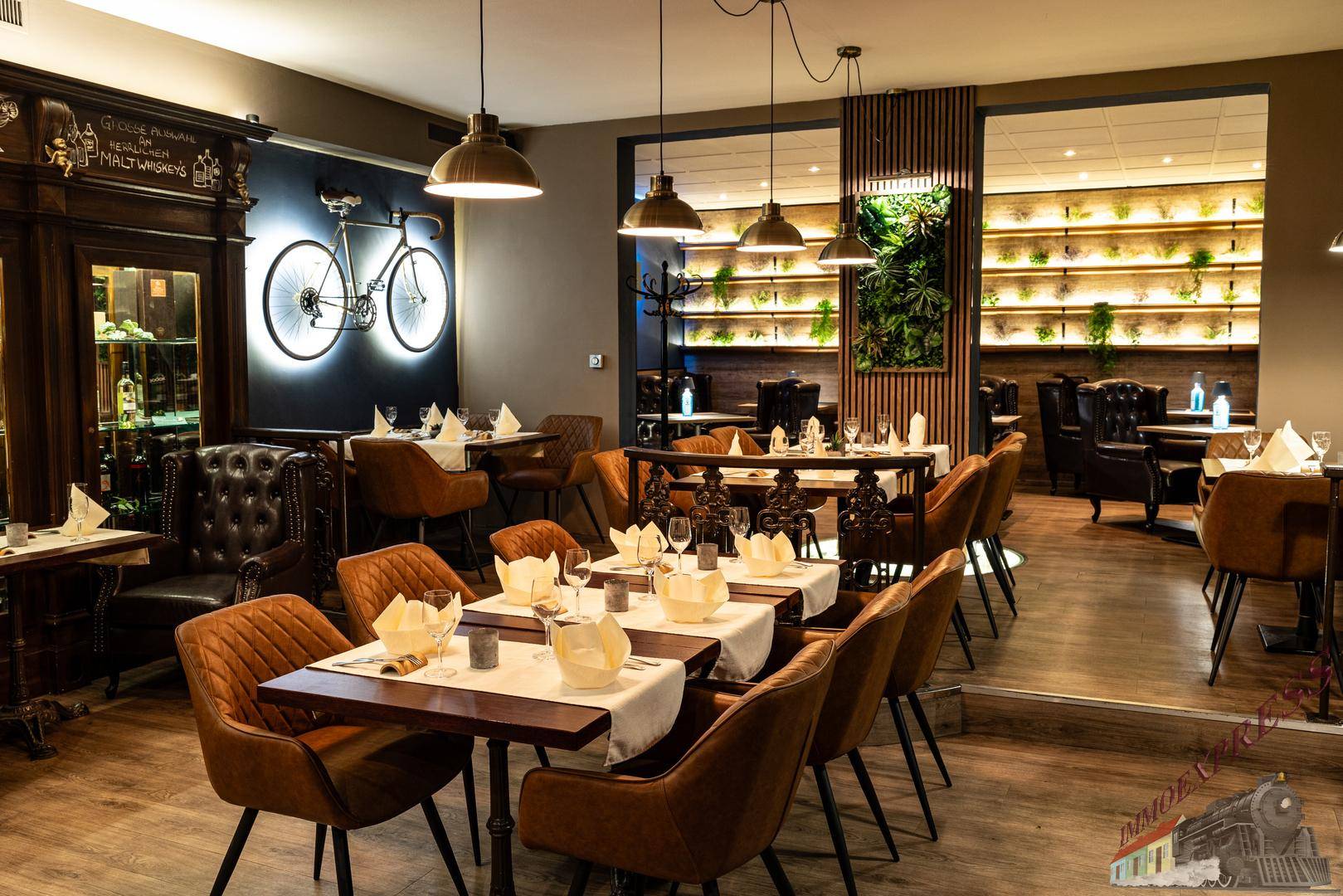 Geräumiger Restaurantbereich mit mehreren Tischen, Holzboden und einer dekorativen grünen Wand.