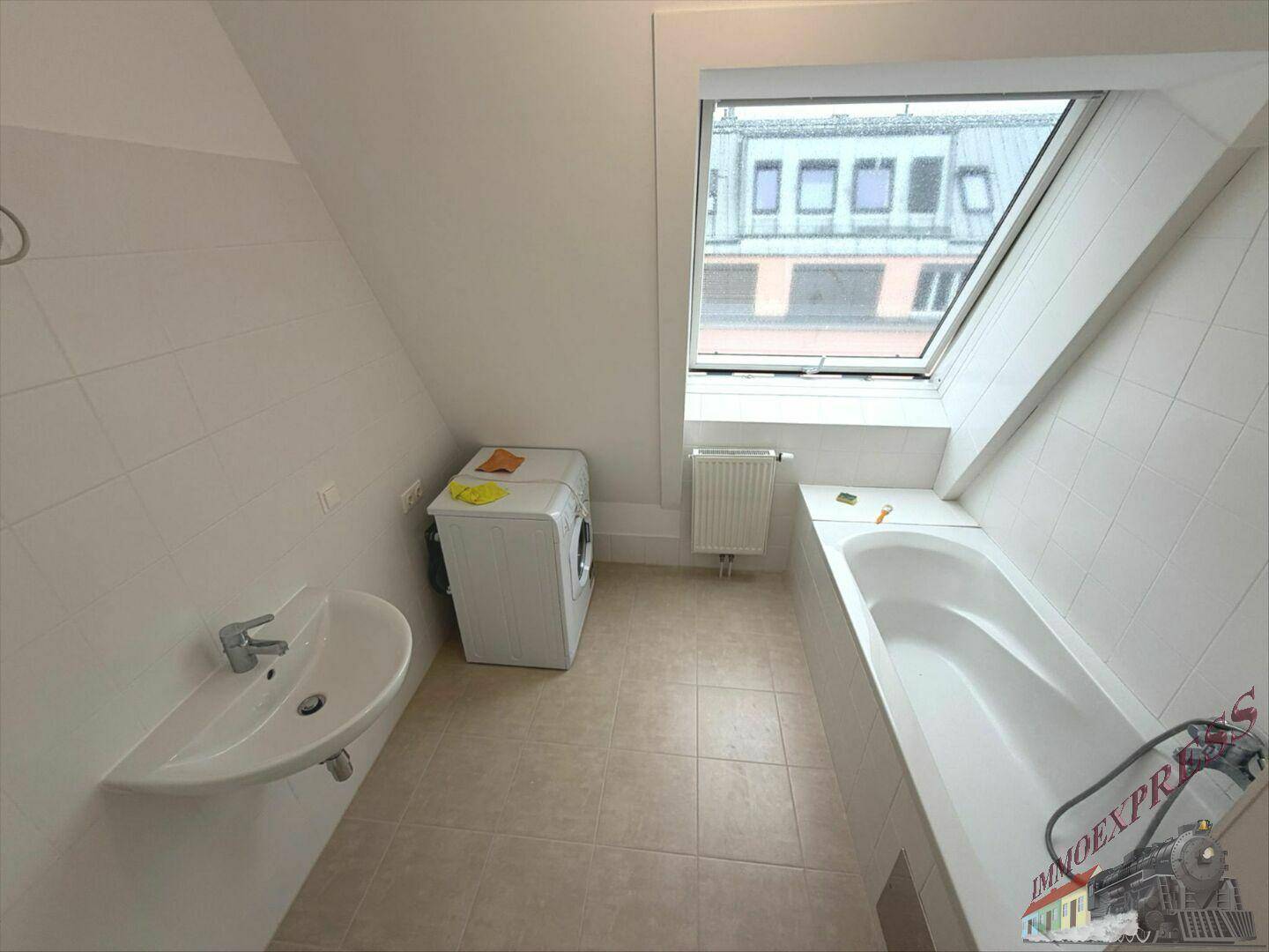 Funktionales Badezimmer mit Waschbecken, Badewanne und Waschmaschine unter einem Dachfenster.