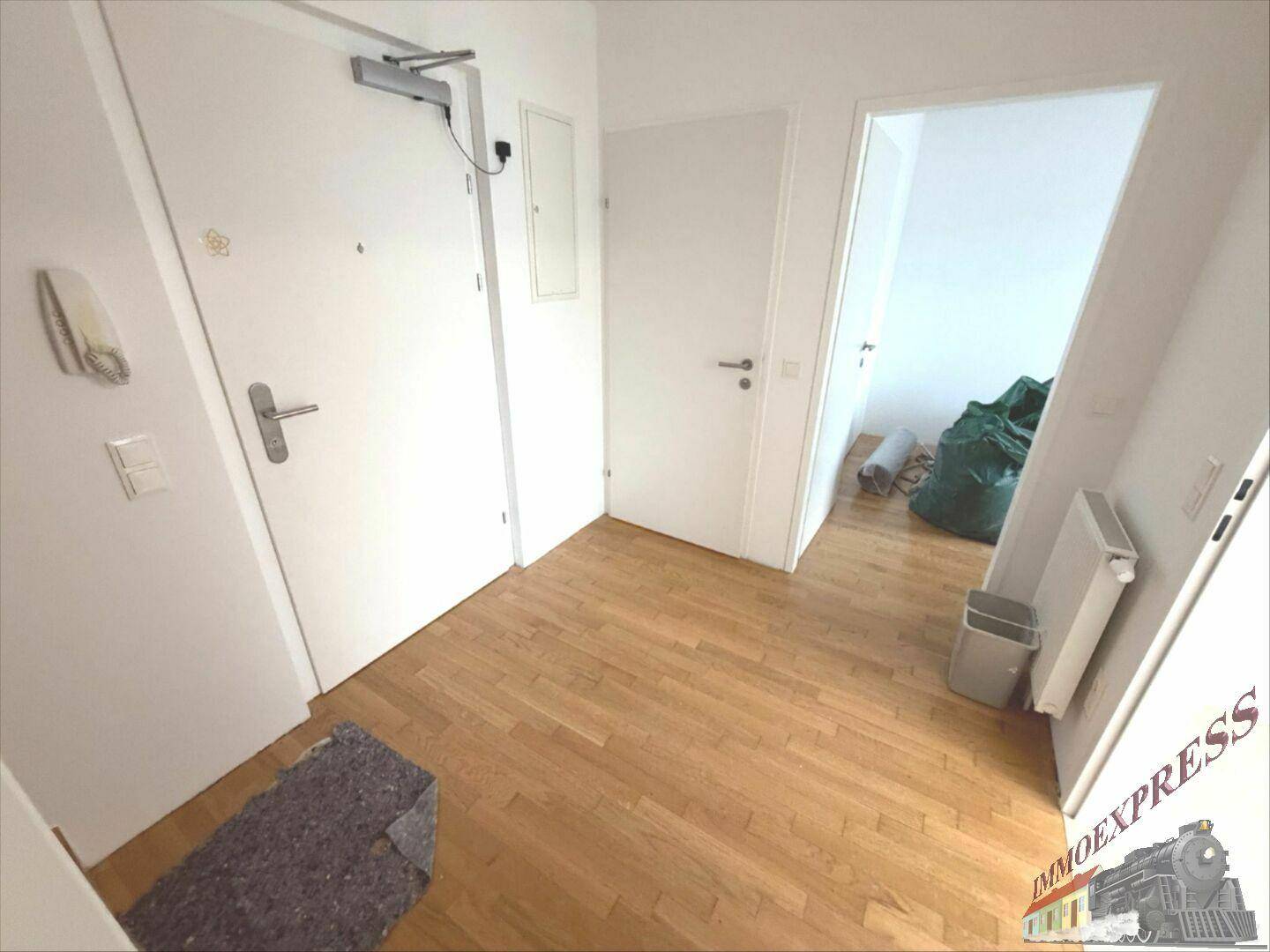 Eingangsbereich mit Holzboden, weißen Wänden und Gegensprechanlage, bietet Zugang zu den Wohnräumen.