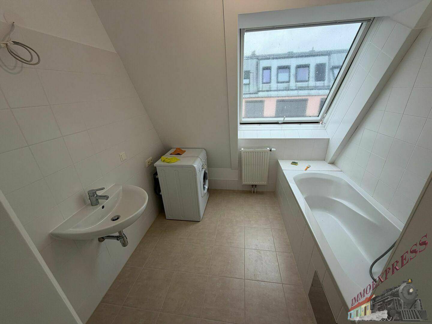 Praktisches Badezimmer mit Waschbecken, Badewanne und Waschmaschine, gut beleuchtet durch ein Dachfenster.