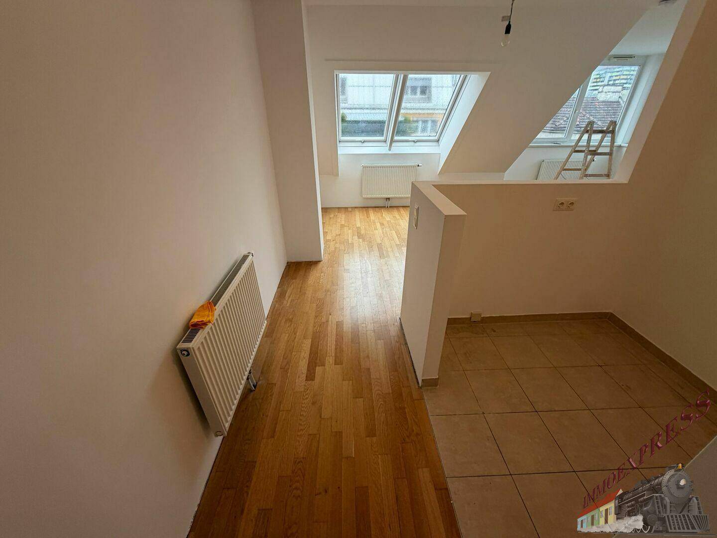 Blick vom gefliesten Bereich über den Holzboden zu den hellen Dachfenstern und Heizkörpern.
