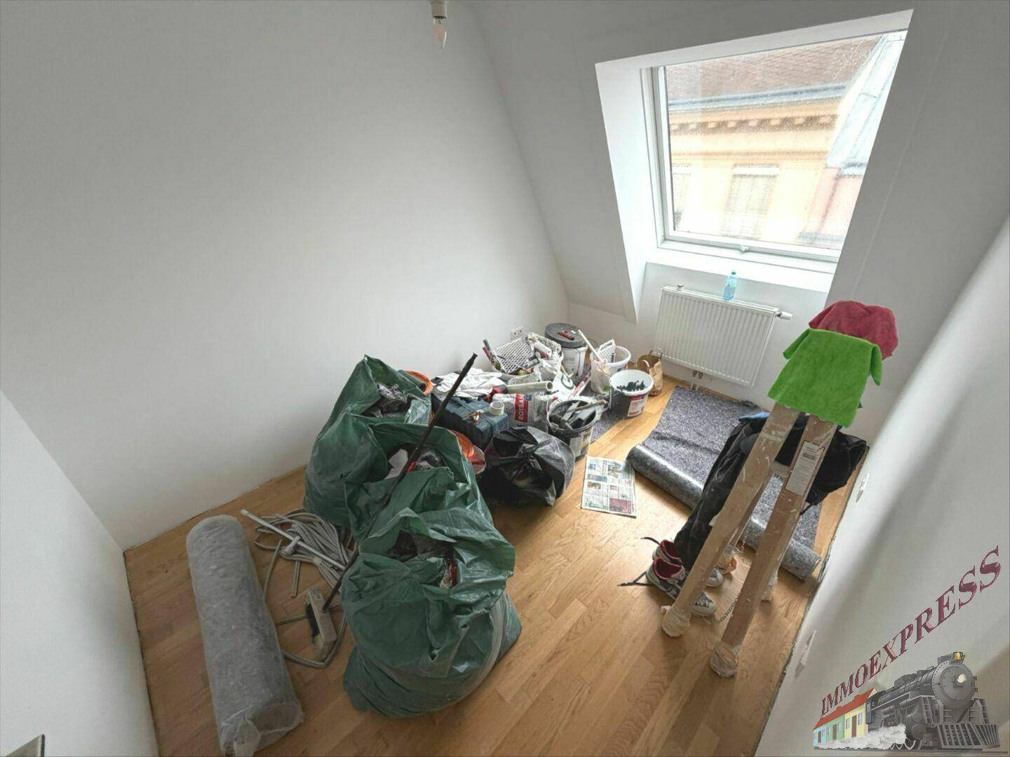 Dachgeschossraum mit Holzboden und Dachfenster, derzeit als Lagerraum für Renovierungsarbeiten genutzt.