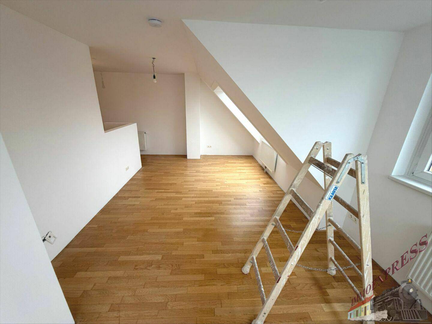 Heller Dachgeschossraum mit Holzboden, schrägen Wänden und einem großen Dachfenster.