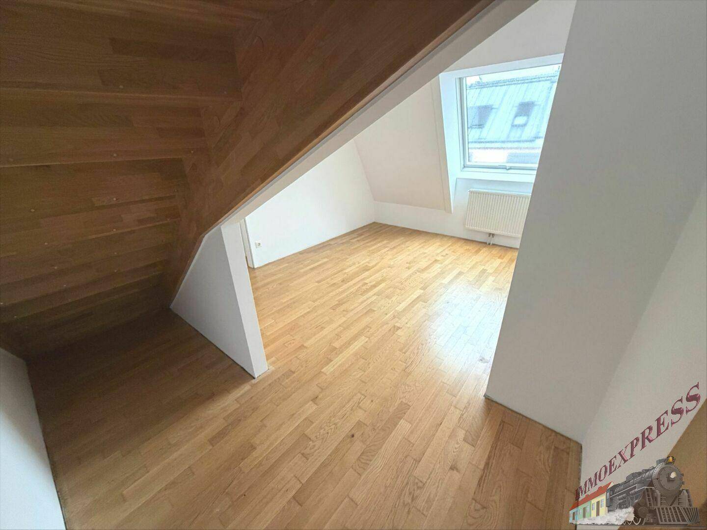 Helles Schlafzimmer im Dachgeschoss mit Holzboden, schrägen Wänden und einem großen Dachfenster.