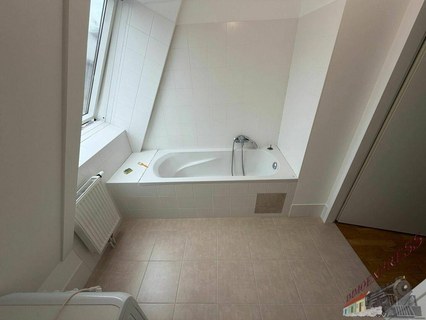 Helles Badezimmer mit eingebauter Badewanne, weißen Fliesen und einem Dachfenster für Tageslicht.