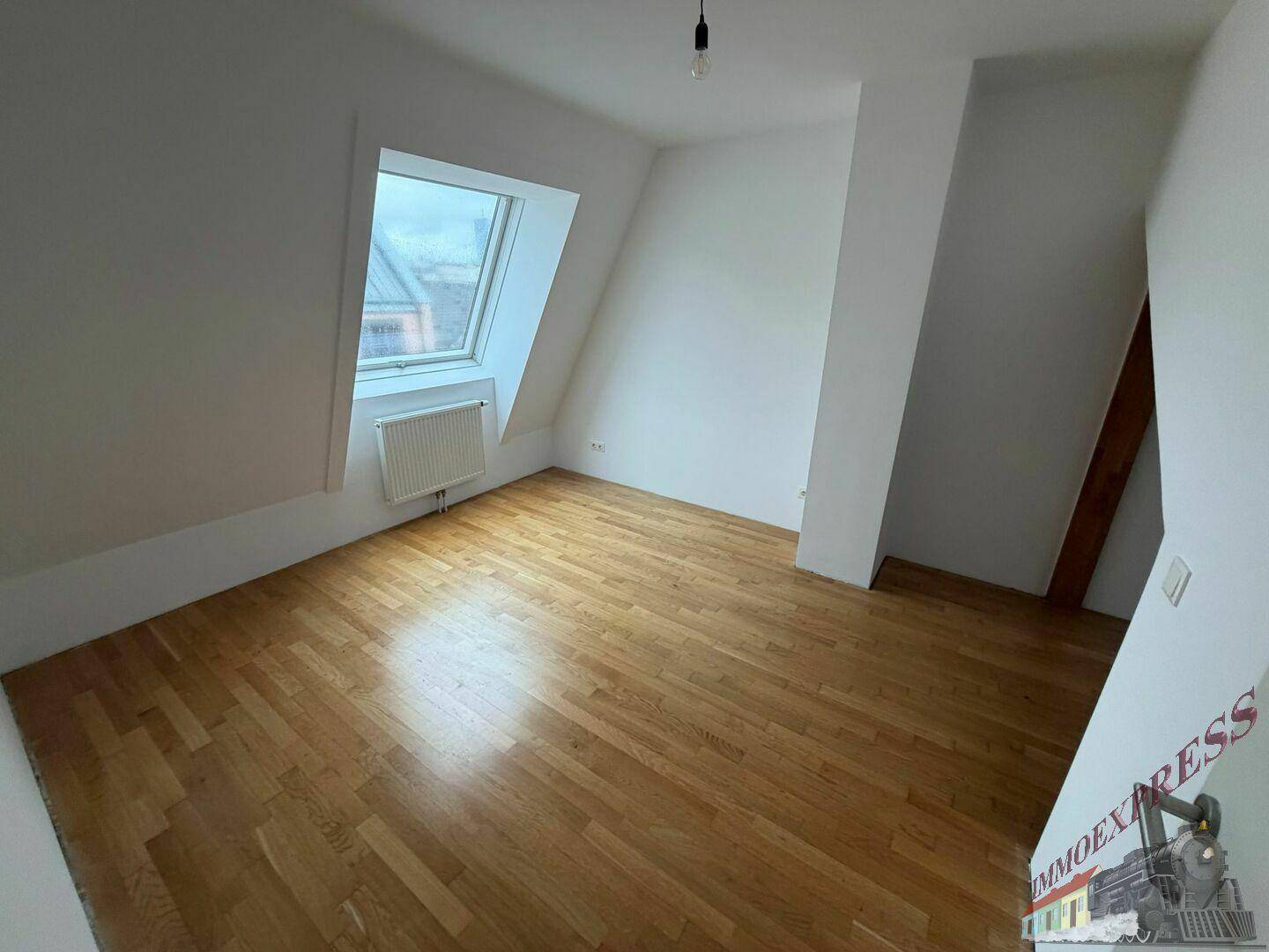Geräumiges Schlafzimmer im Dachgeschoss mit Holzboden und viel Tageslicht durch das große Dachfenster.