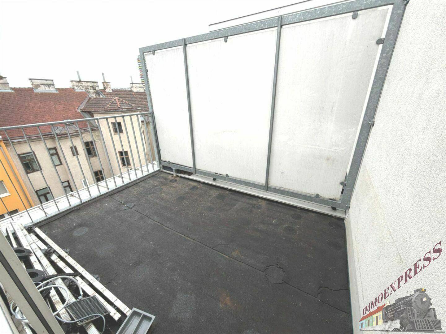 Kleiner Balkon mit Metallgeländer und Sichtschutz, bietet einen Blick auf die umliegenden Gebäude.