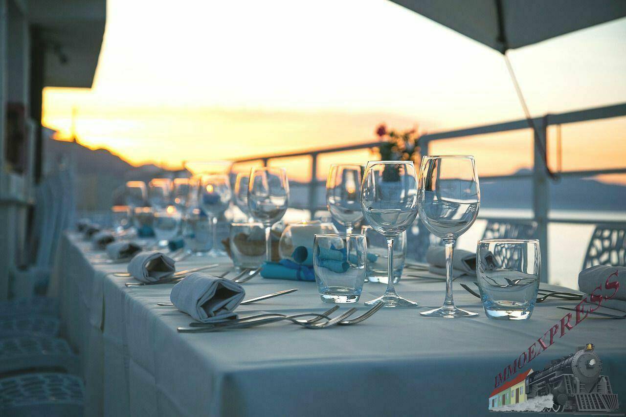 Ein langer, gedeckter Tisch auf einer Terrasse mit Blick auf das Meer bei Sonnenuntergang.