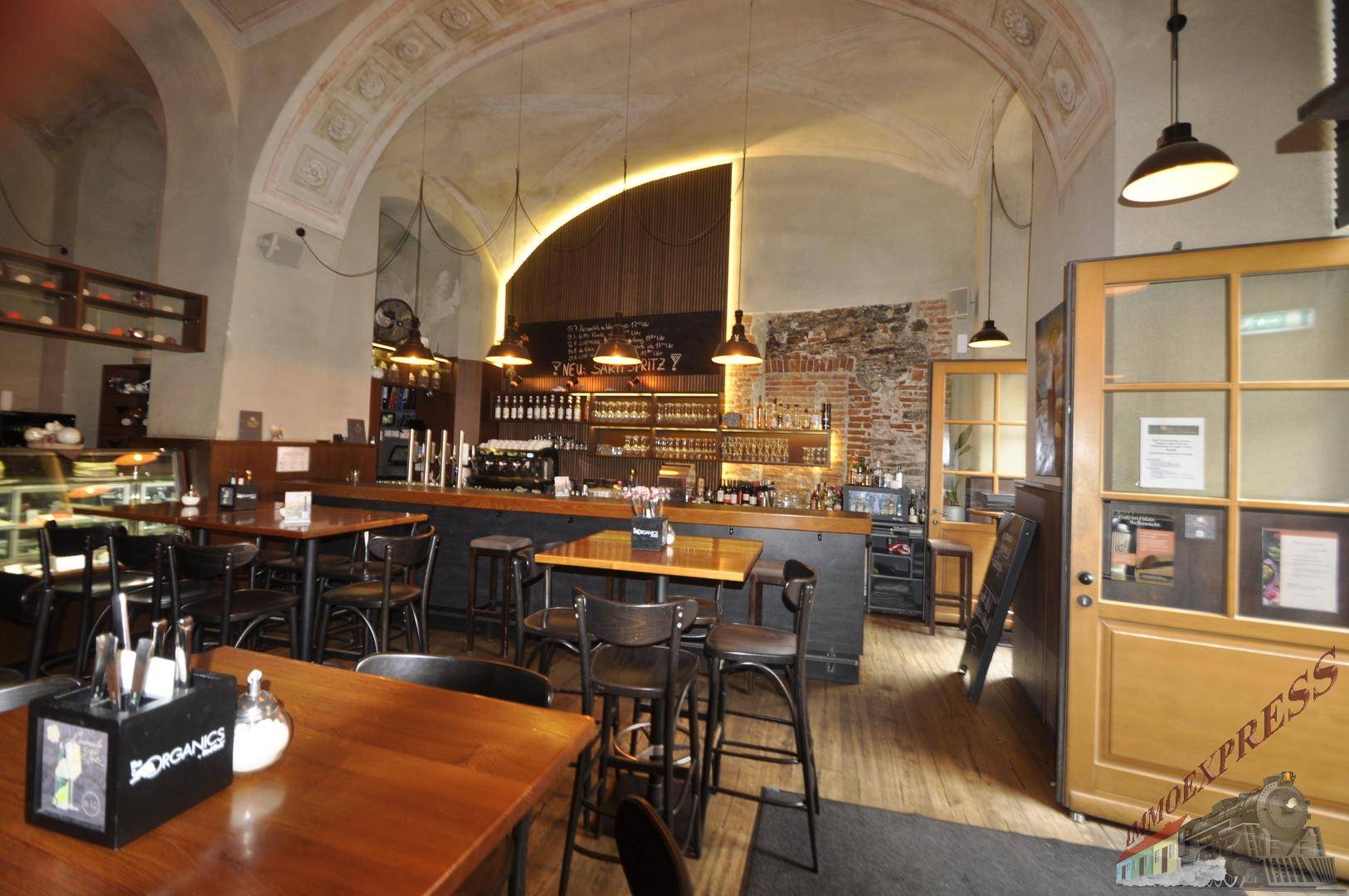 Geräumiger Barbereich mit Holztischen, Stühlen und einer langen Theke unter einem Gewölbedach.