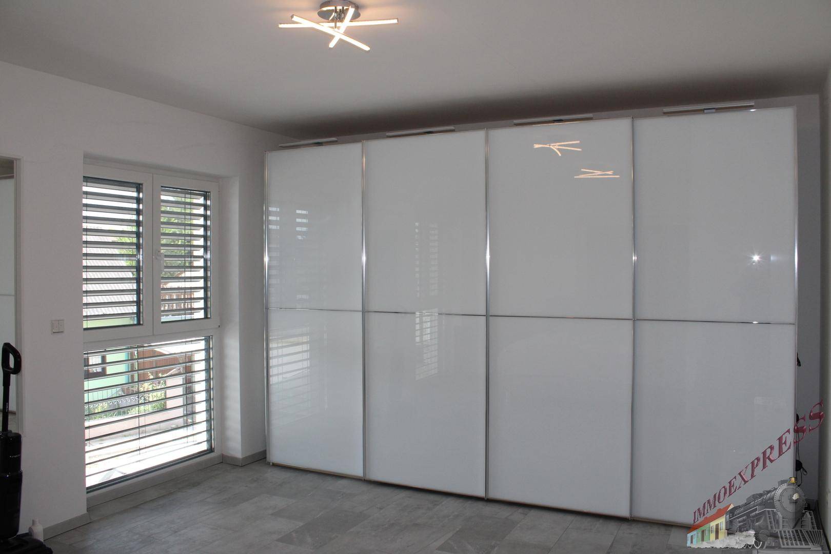 Schlafzimmer mit großem, weißen Hochglanz-Einbauschrank und Fenster mit Jalousien.