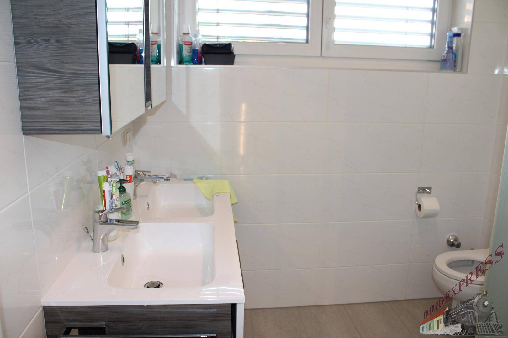 Modernes Badezimmer mit Doppelwaschbecken, Spiegelschrank, Toilette und weißen Fliesen.
