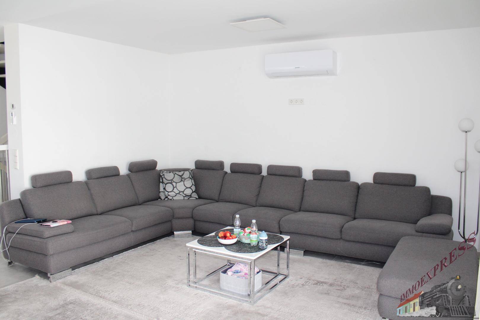 Geräumiges Wohnzimmer mit großem grauen Ecksofa, Couchtisch und Klimaanlage an der Wand.