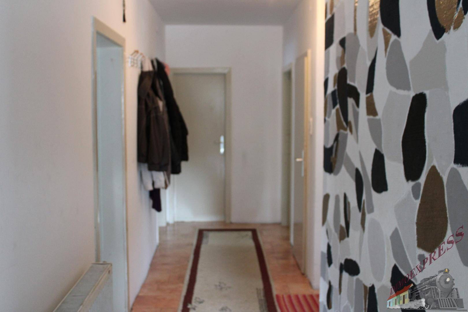 Langer Flur mit gemusterter Tapete und Garderobe, führt zu weiteren Räumen.