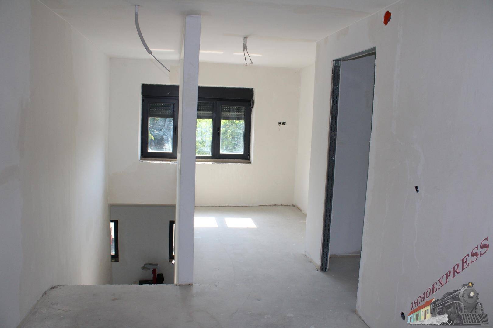 Unfertiger Flurbereich mit Treppenabgang und Fenster, bereit für den Innenausbau.