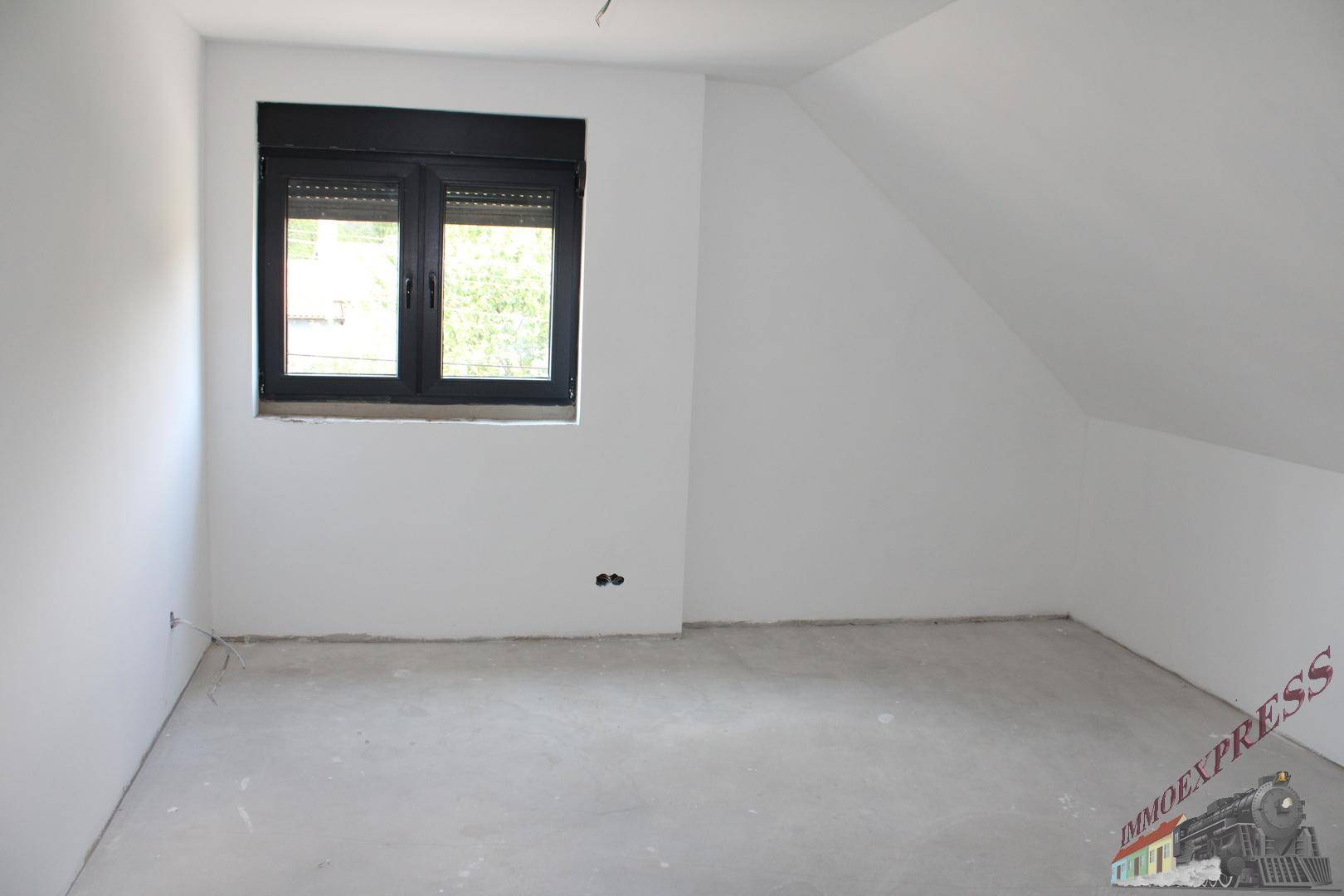 Unfertiger Raum im Dachgeschoss mit schrägen Wänden und Fenster mit Rollladen.