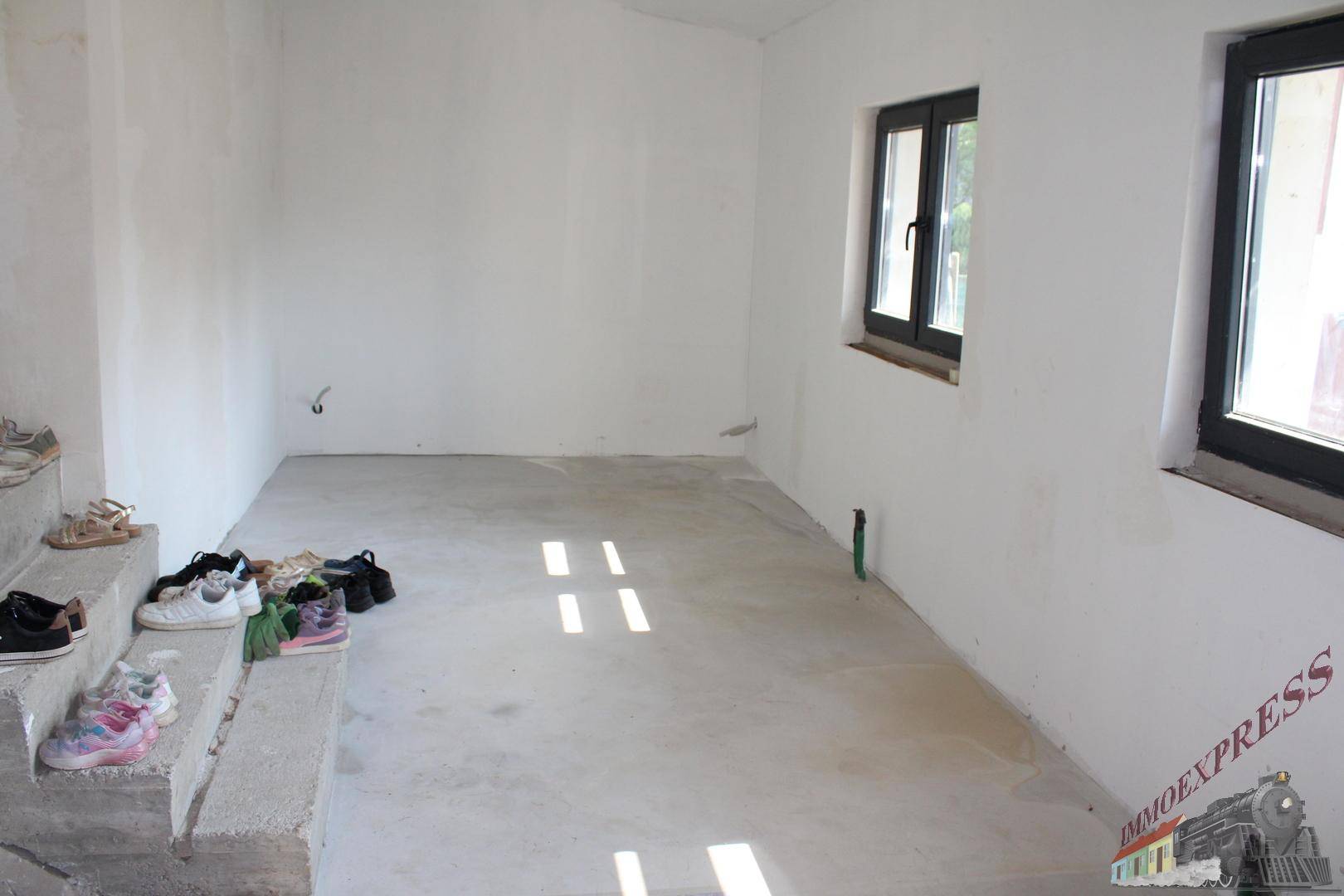 Unfertiger Raum mit Betonboden und zwei Fenstern, bereit für den Ausbau.