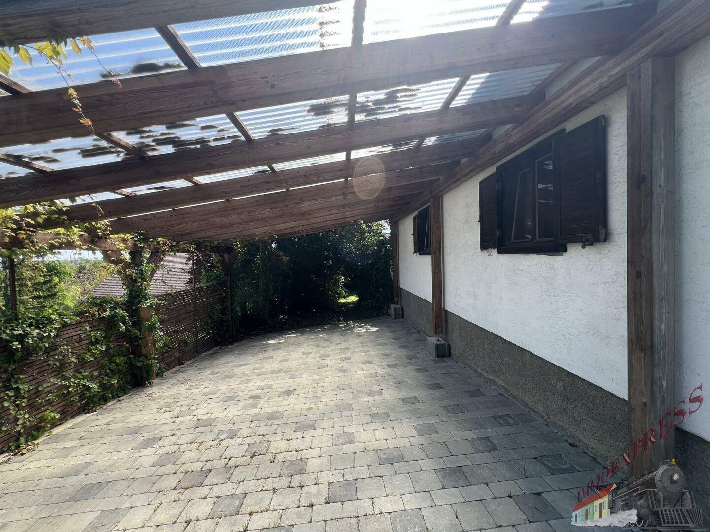 Überdachter Stellplatz oder Carport mit transparentem Dach und gepflastertem Boden.
