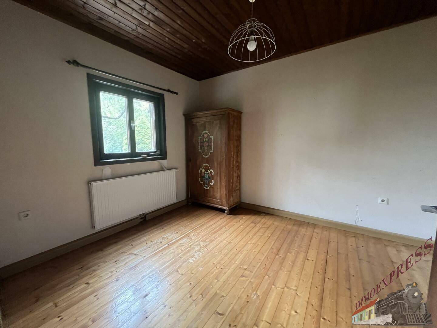 Schlafzimmer mit Holzdielenboden, Holzdecke und einem antiken Holzschrank.