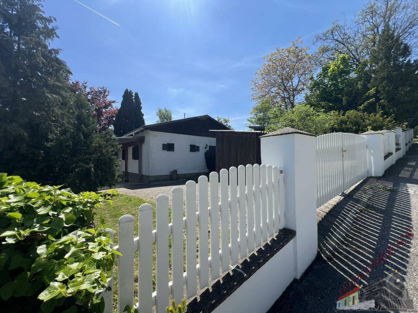 Eingangsbereich des Grundstücks mit weißem Zaun und Blick auf das dahinterliegende Haus.