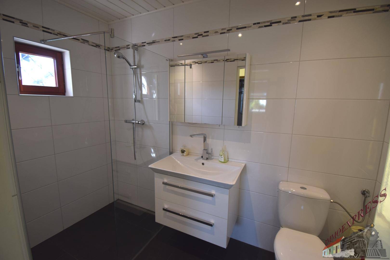 Modern gefliestes Badezimmer mit ebenerdiger Dusche, Waschbecken und Spiegelschrank, hell und sauber.