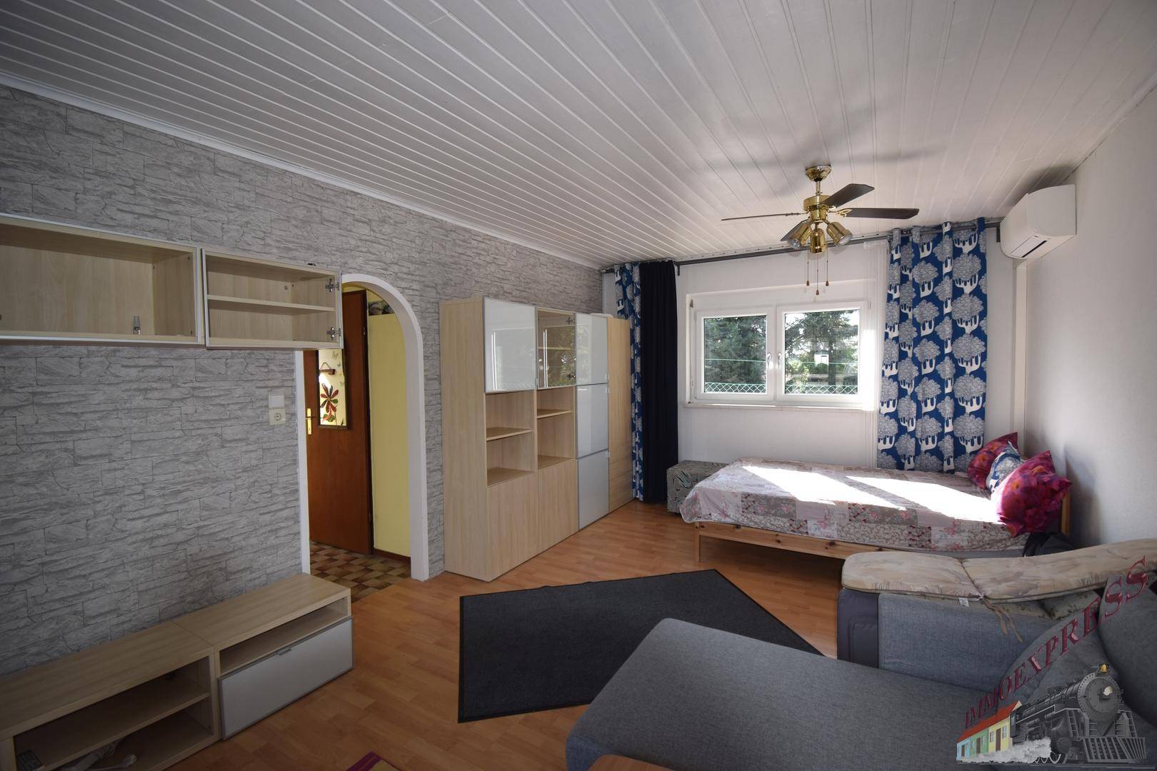 Gemütliches Wohnzimmer mit Holzboden, strukturierten Wänden und einem Deckenventilator, hell beleuchtet.