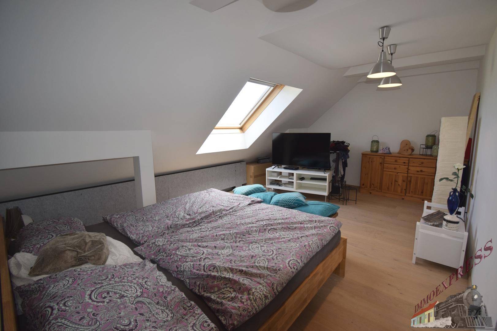 Schlafzimmer im Dachgeschoss mit Doppelbett, Dachfenster und Holzboden.