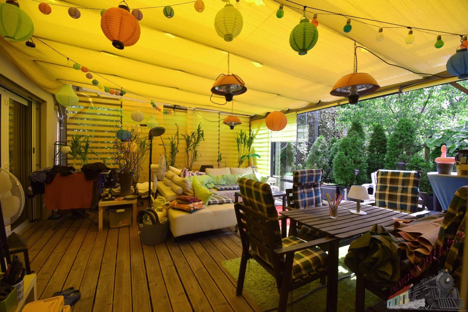 Überdachte Terrasse mit Holzboden, Sitzgelegenheiten und bunter Dekoration.