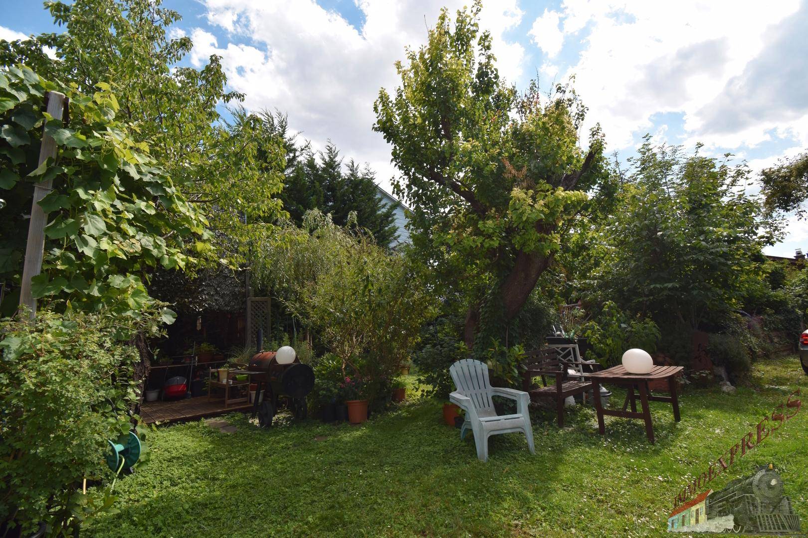 Großer Garten mit Rasenfläche, Bäumen und einer kleinen Sitzecke im Freien.